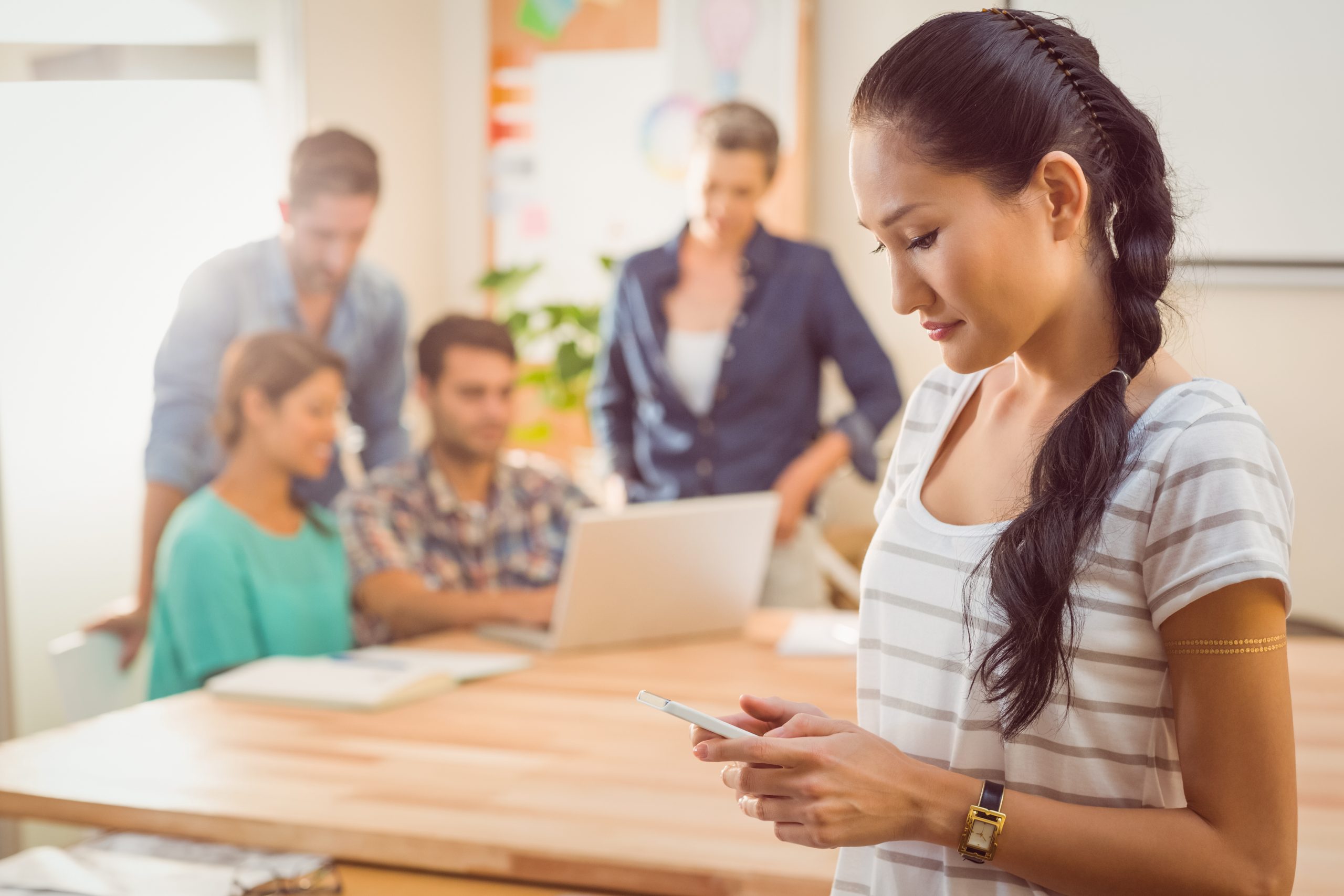 Young businesswoman using her phone while her team is working