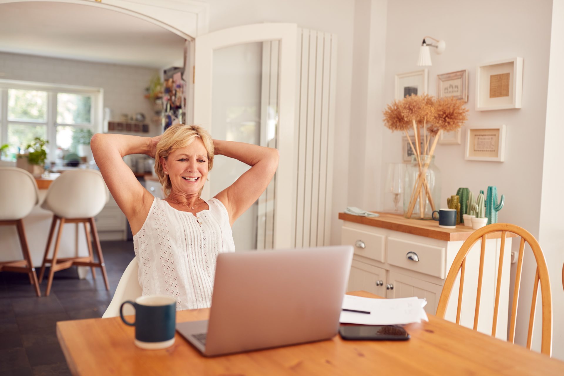Retired Woman At Home In Kitchen Happy With Sense Of Achievement At End Of Day Working On Laptop
